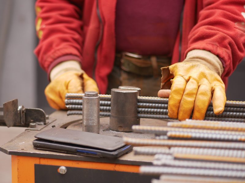 Construction Worker Using Metalwork Equipment on Steel Rods at Worksite